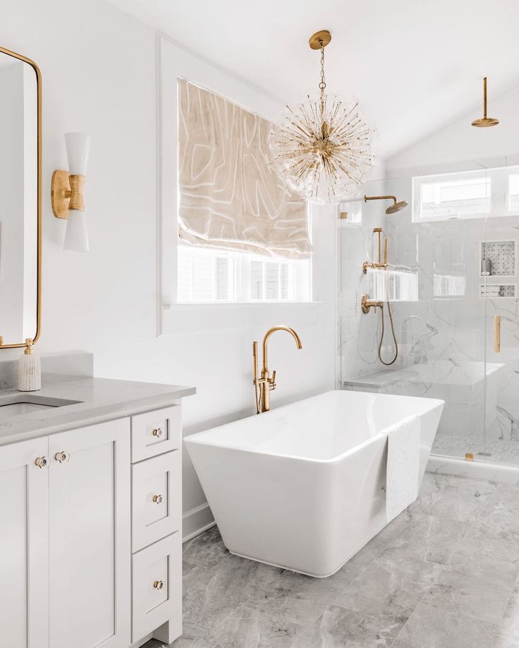 a white bath tub sitting next to a sink under a bathroom mirror with gold fixtures