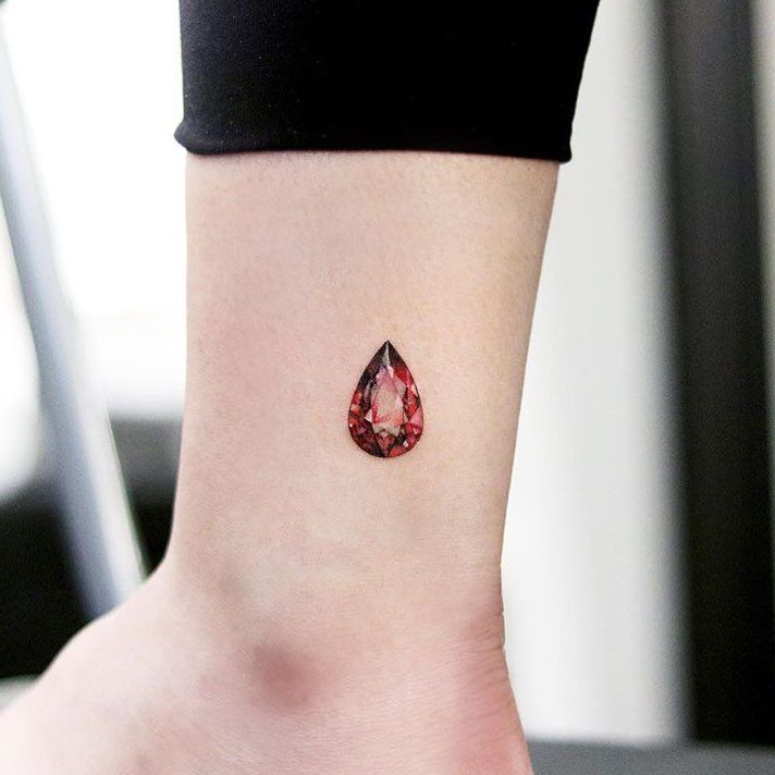 a woman's ankle with a small red tear shaped tattoo on her left foot