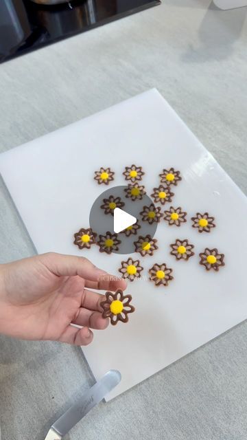 a person is making cookies on a white board with yellow and brown decorations in the shape of flowers