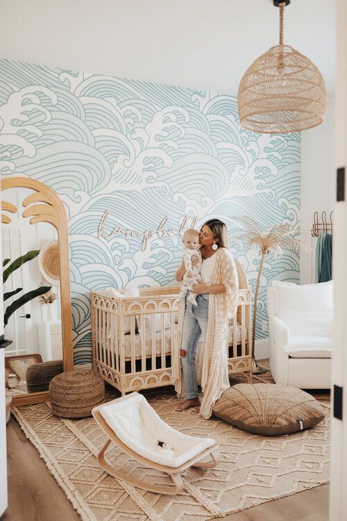 a woman standing in front of a crib holding a baby next to a mirror