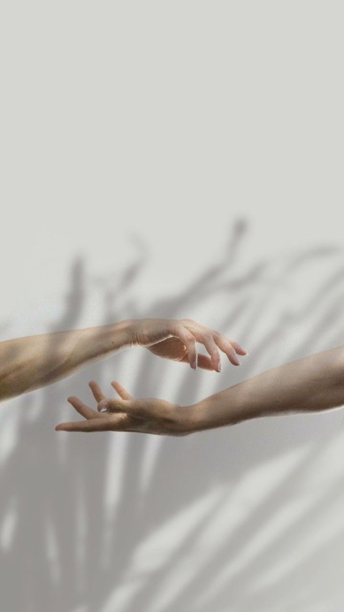 two hands reaching out towards each other in front of a white wall with shadows on it