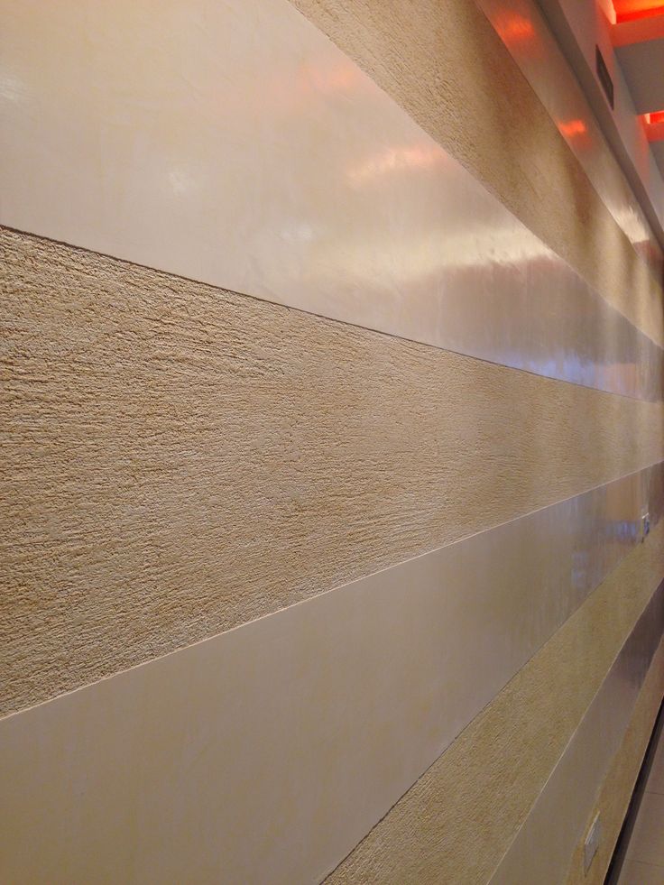 a man walking down a hallway next to a wall with light colored wood panels on it