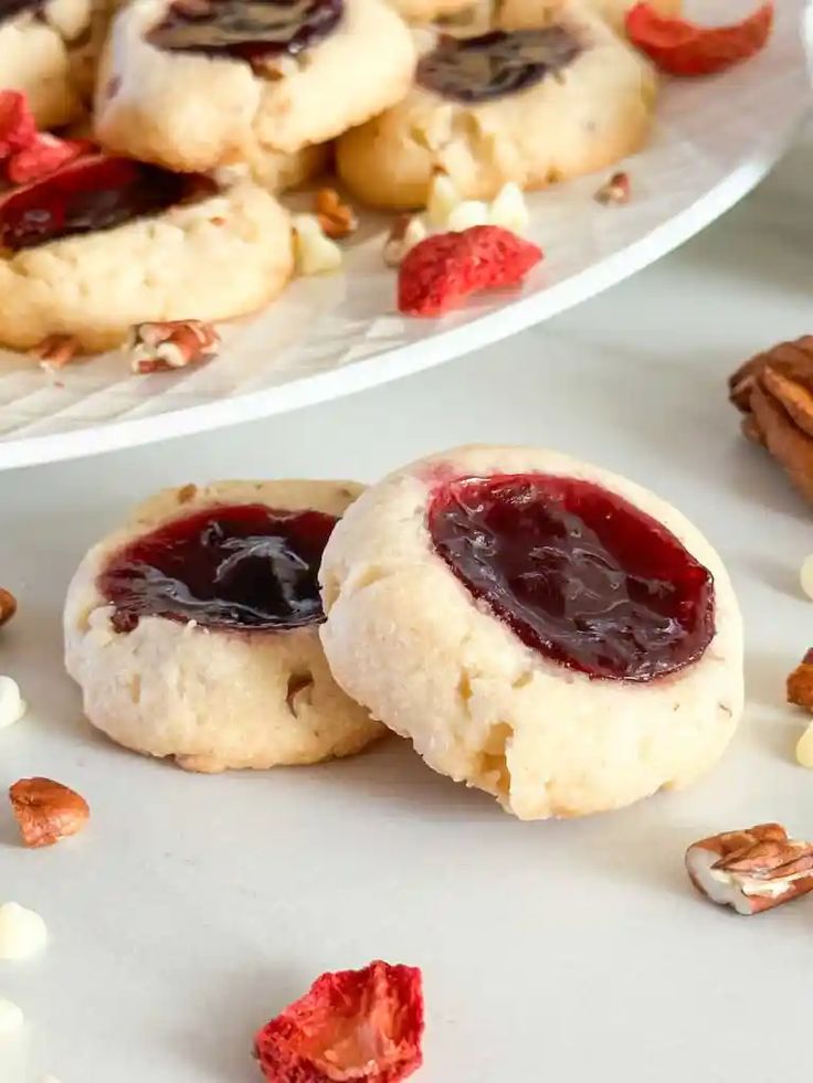 two cookies with jam and nuts on the side next to a plate of pecans