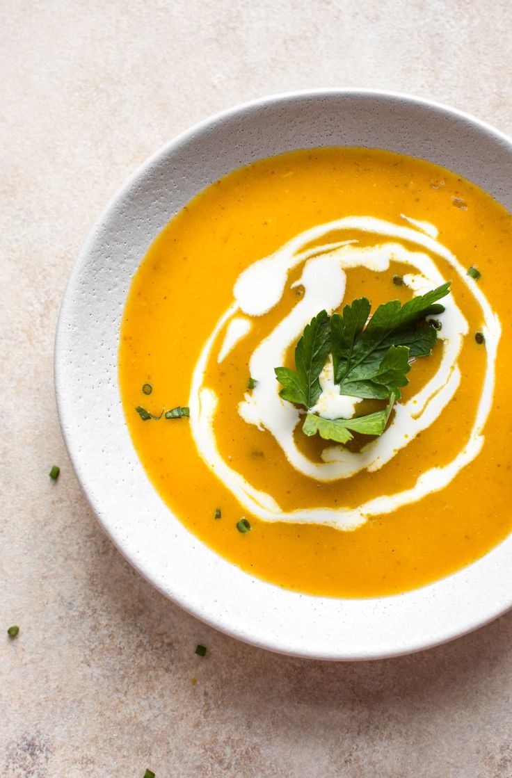 a white bowl filled with carrot soup topped with sour cream and garnished with parsley