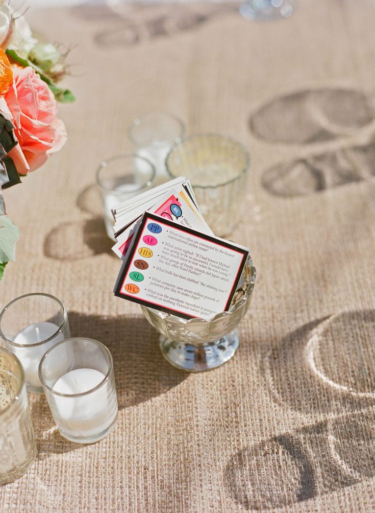 a table topped with glasses filled with water and cards next to vases full of flowers