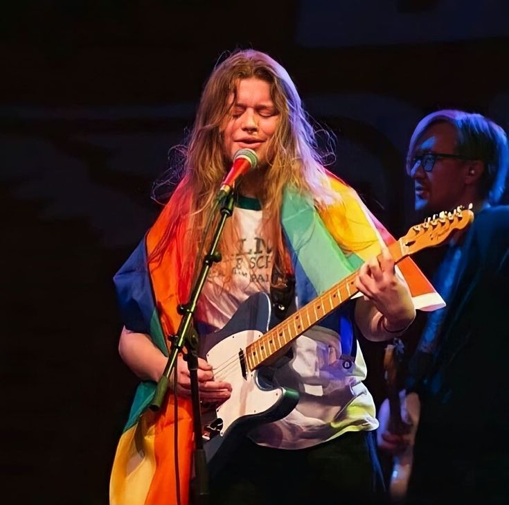 a man standing in front of a microphone while holding a guitar