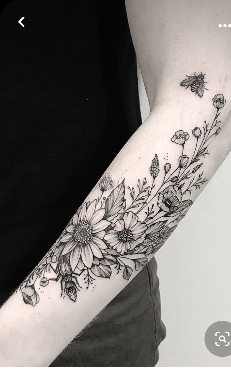 a black and white flower tattoo on the left arm, with butterflies flying around it