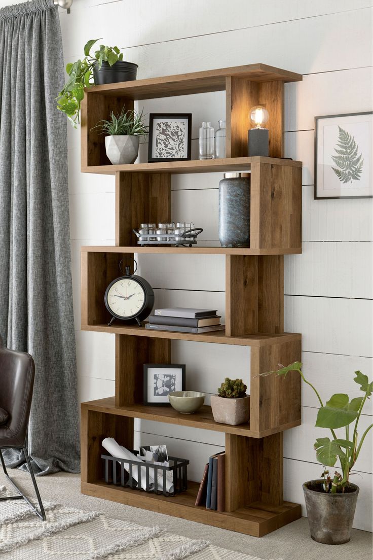 a wooden shelf with various items on it in front of a window and a chair