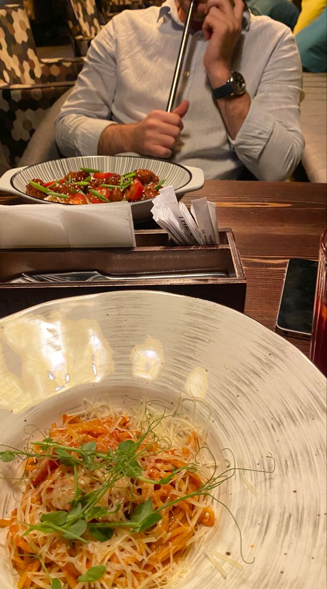 a man sitting at a table with plates of food in front of him on his phone