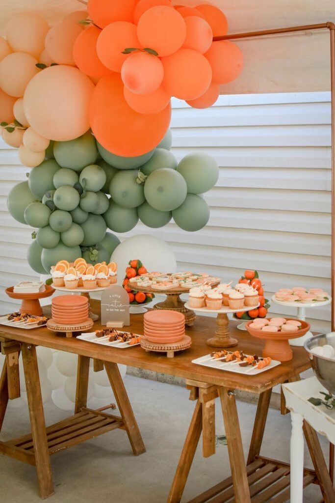 a table topped with cakes and cupcakes next to a bunch of balloons hanging from the ceiling