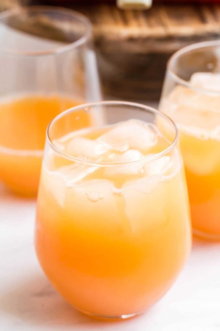 three glasses filled with orange juice sitting on top of a table next to some bread