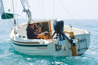 a man sitting in the cockpit of a sailboat waving to someone on the deck