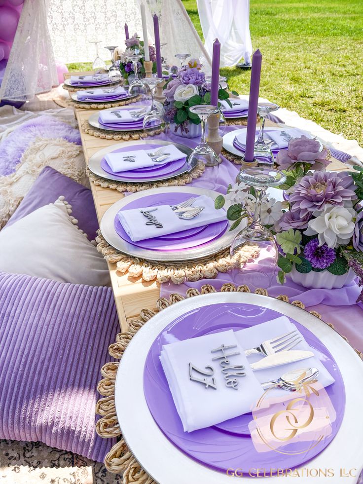 the table is set with purple and white plates, napkins, silverware, and flowers