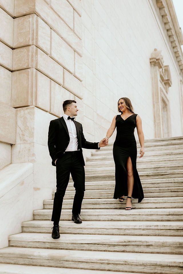 a man and woman in formal wear walking up some steps together, holding hands with each other