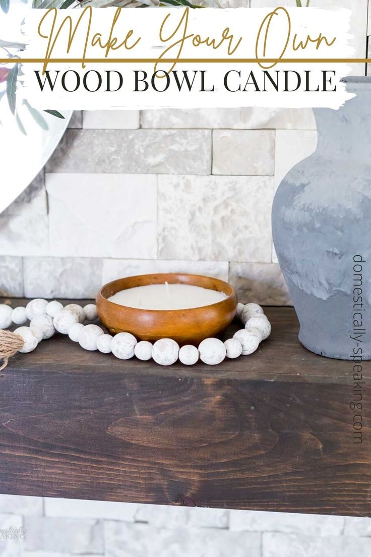 a wooden bowl candle sitting on top of a table next to a vase with flowers