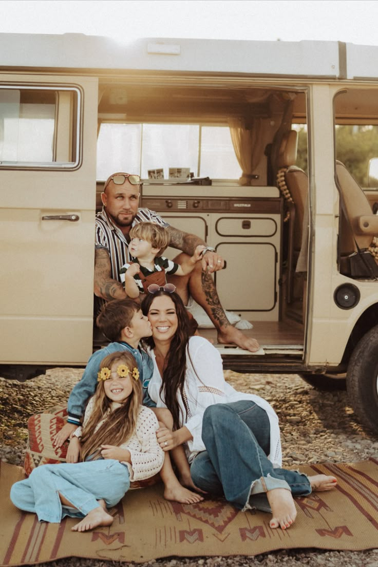 a group of people sitting on top of a rug in front of a camper