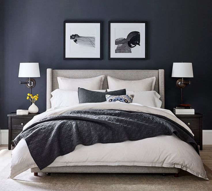 a bedroom with blue walls and white bedding, two framed pictures above the bed