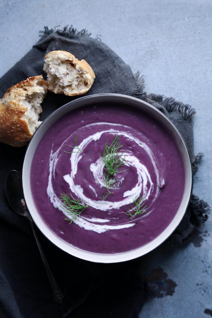 a bowl filled with purple soup next to a piece of bread