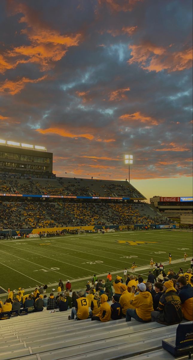 a football stadium filled with lots of people sitting on the bleachers at sunset