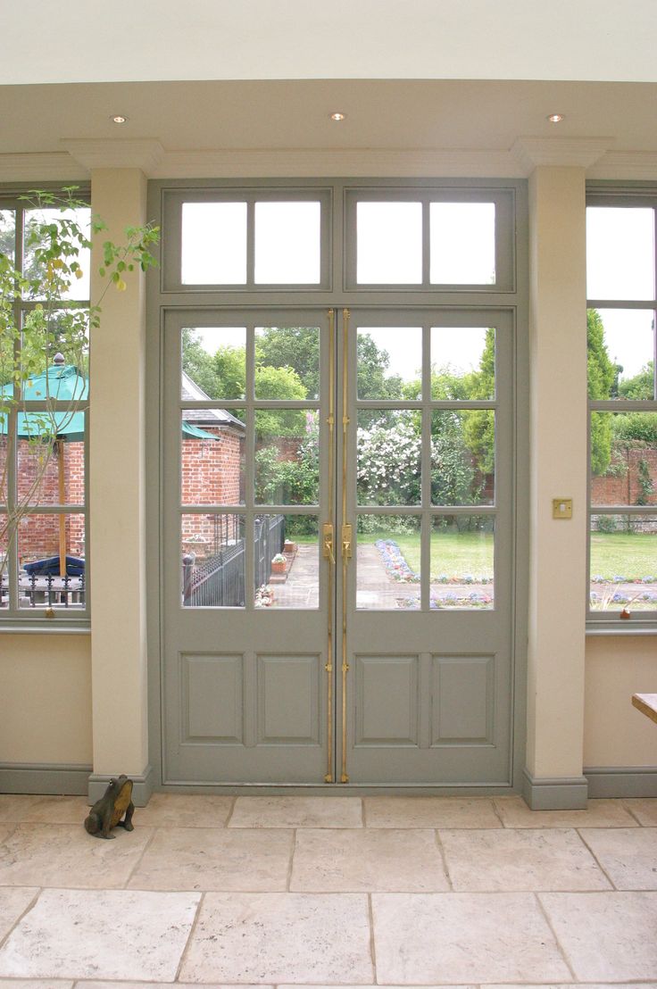 two cats sitting on the floor in front of double doors that lead to a patio