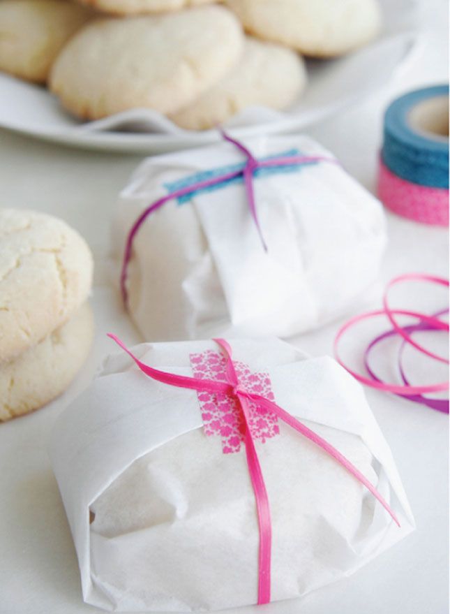 some cookies wrapped in white paper and tied with pink ribbon on top of a table