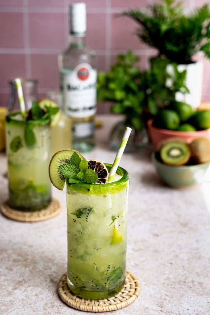 two glasses filled with green drinks sitting on top of a counter next to potted plants