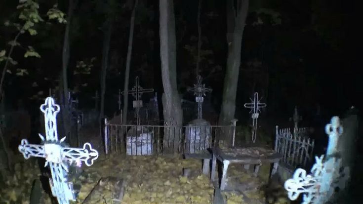 an old cemetery at night with crosses and tombstones on the ground in front of it