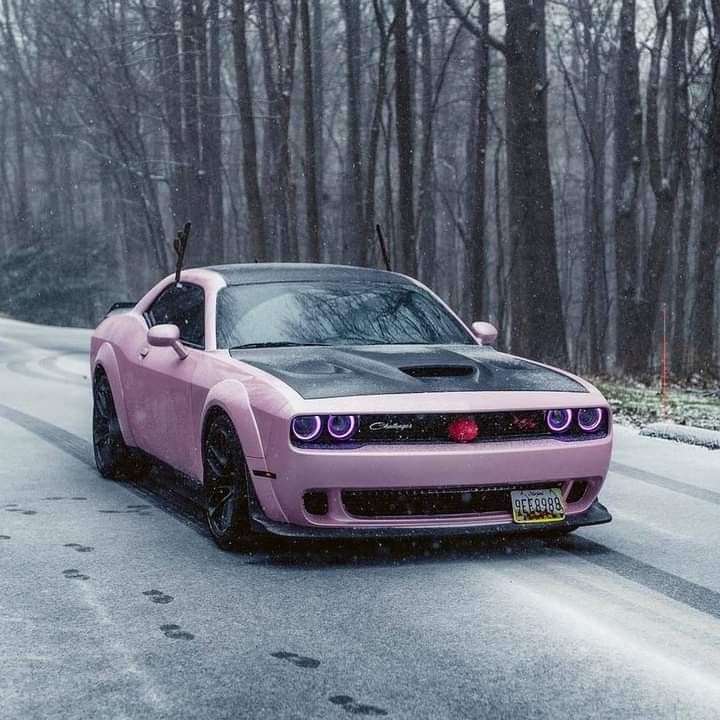 a pink car parked on the side of a road in front of snow covered trees