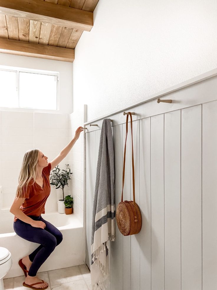 a woman is sitting on the toilet and reaching up to grab something from the wall