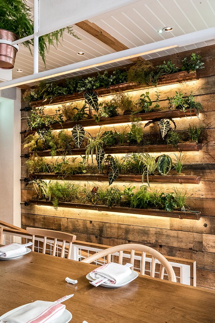 a wooden table topped with lots of plants next to a wall filled with greenery