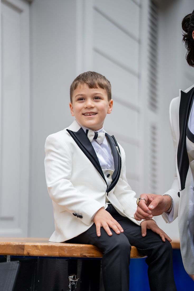 Elevate your child's style with the Radiant White Boy's Tuxedo, a charismatic choice designed to stand out. Combining impeccable taste with effortless elegance, this tuxedo ensures your little one leaves an unforgettable, dapper impression on any occasion. From HolloMen Spring Summer Collection. Tuxedo Color: White. Available sizes are from 5 to 14 years boys. It is expertly crafted from a luxurious blend of 55% Cotton and 45% Polyester. This suit is a Slim fit for a tailored look, and it features a Double slit, Single Button, and Full Lining seamlessly integrated for a sleek design. To maintain the premium quality of your Black Tuxedo Suit, dry clean only. Kid Tuxedo, Boys Tuxedo, White Tuxedo, Suit Material, Tuxedo Suit, Jacket Vest, Peak Lapel, Kids Collection