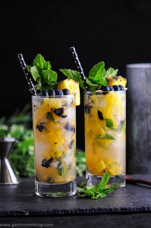 two glasses filled with lemonade and blueberries on top of a table next to a cocktail shaker