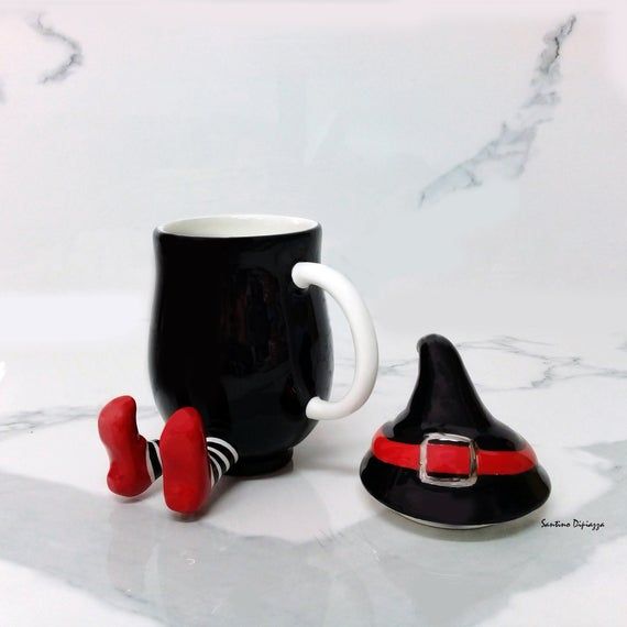 a black coffee mug with red handles and a gnome's hat next to it