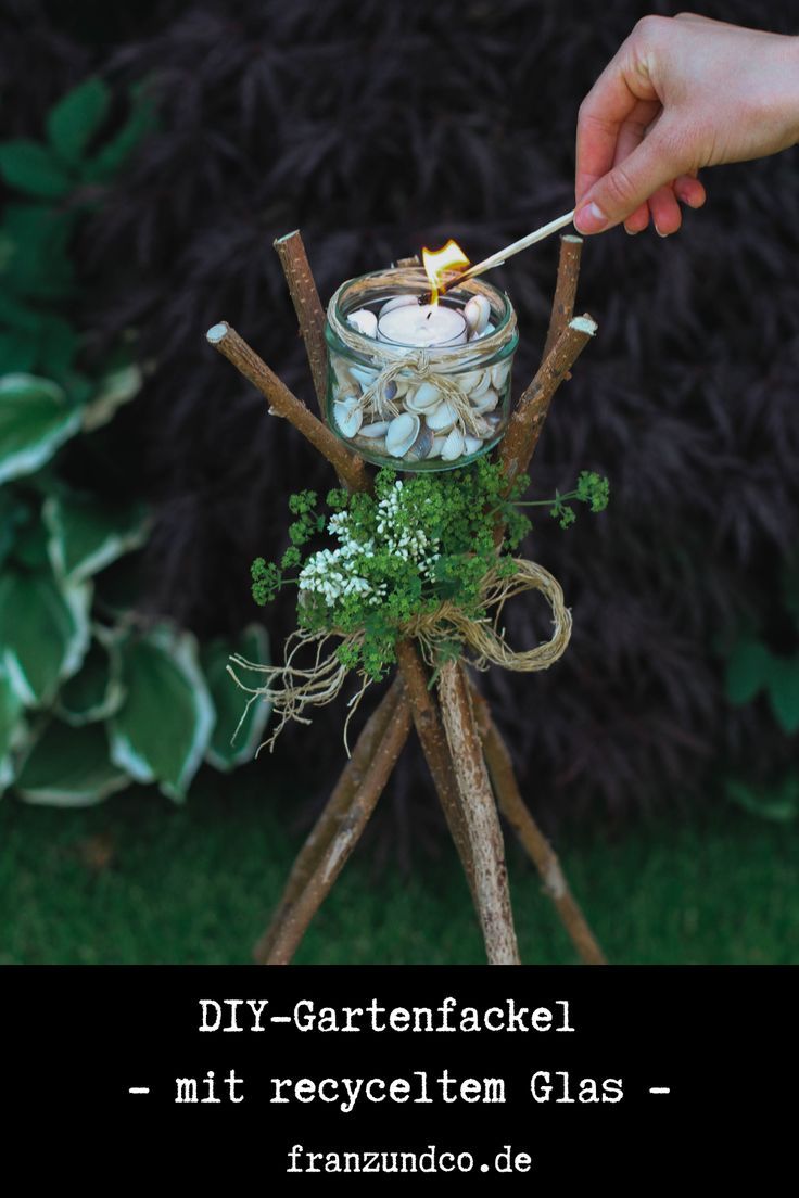 a person lighting a candle in a glass jar on top of a stand made out of sticks