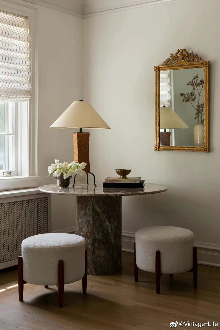 a table with two stools and a lamp in a room next to a window