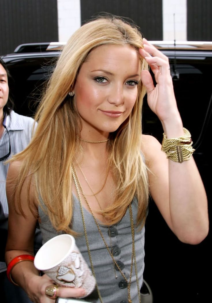 a beautiful young blond woman standing next to a black car