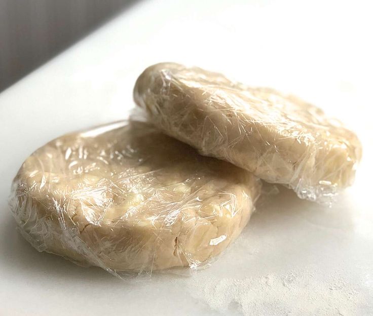 two uncooked doughnuts wrapped in plastic on top of a white counter