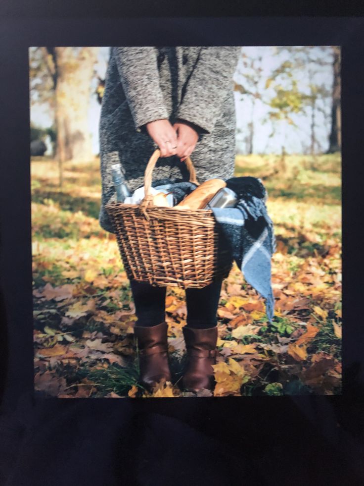 a woman holding a basket full of food in the park with leaves on the ground