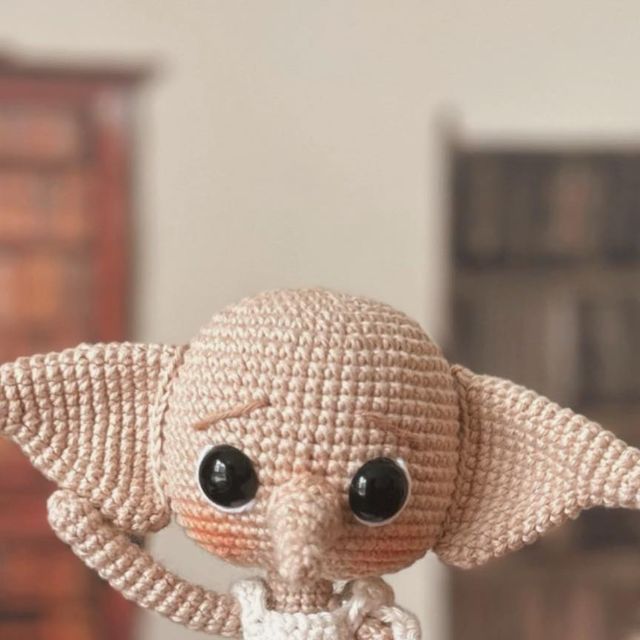 a small crocheted elephant doll sitting on top of a wooden table next to a dresser