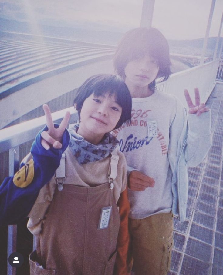 two young people standing next to each other on a bridge with their fingers in the air