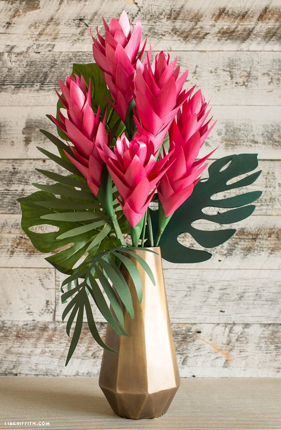 pink flowers are in a gold vase on a wooden table next to a wood wall