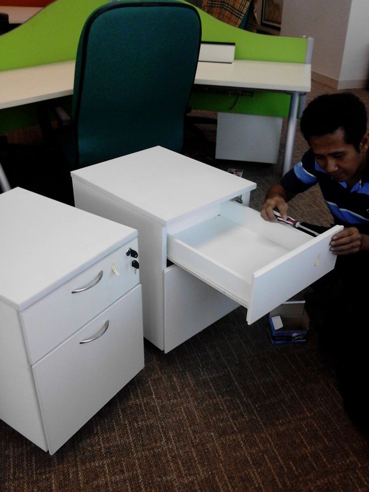 a man sitting on the floor next to two white desks