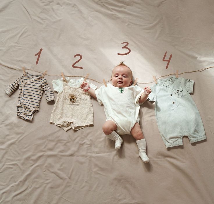 a baby laying on top of a bed next to three other ones hanging from clothes line