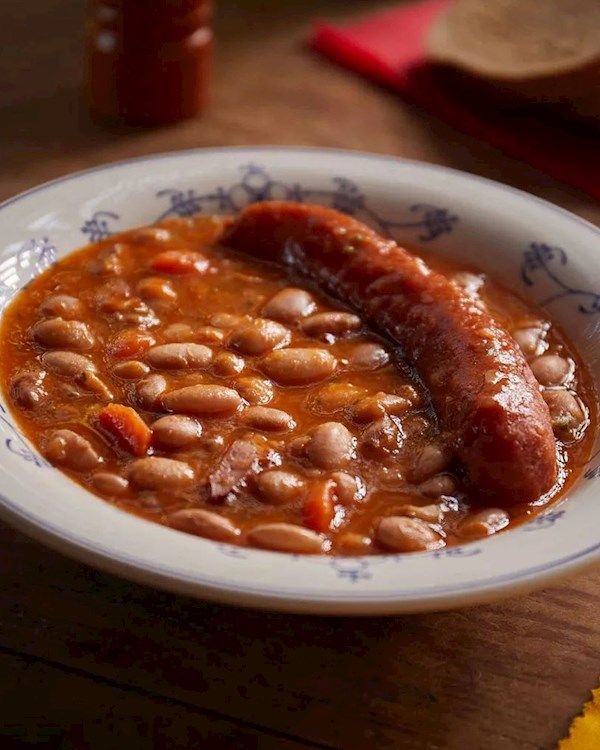 a bowl filled with beans and sausage on top of a wooden table