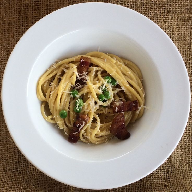 a white bowl filled with pasta and meat on top of a brown cloth covered table