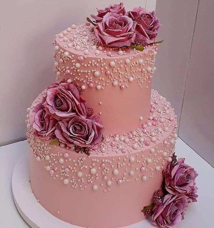 a three tiered cake with pink frosting and purple flowers on the top layer