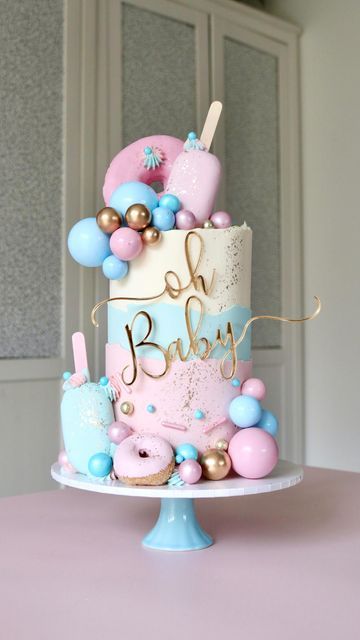 a pink and blue baby shower cake with balloons on it's top, sitting on a table