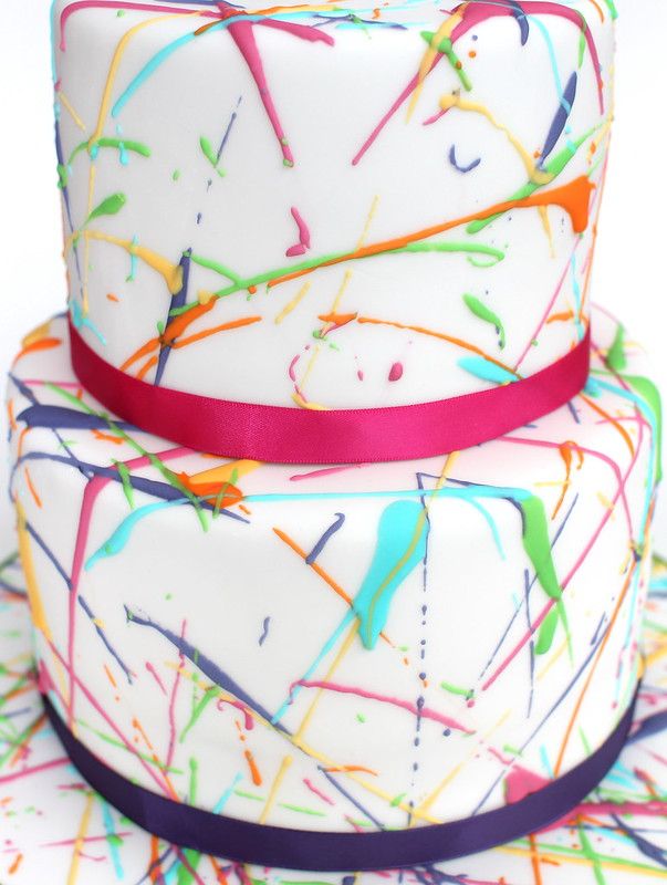 a multi - layer cake with splattered icing on it and a ribbon around the edge