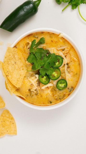 a bowl of soup with tortilla chips and green peppers next to it on a white surface