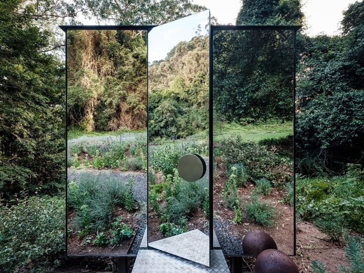 an outdoor area with mirrors and plants in the foreground, surrounded by wooded areas